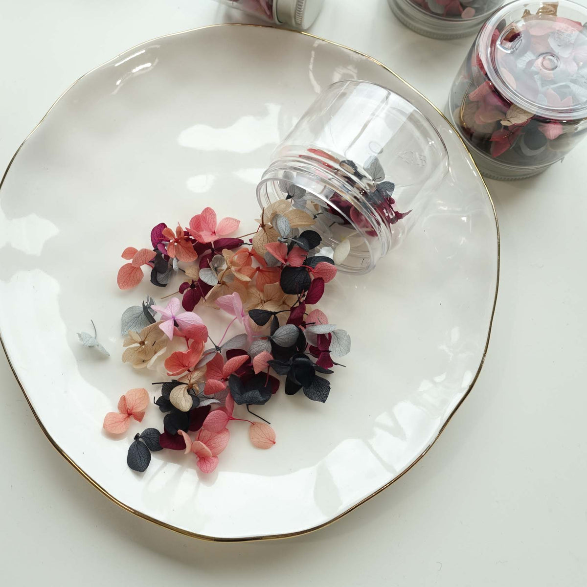 Dried hydrangea petals in pink, burgundy and navy spilling from a glass jar