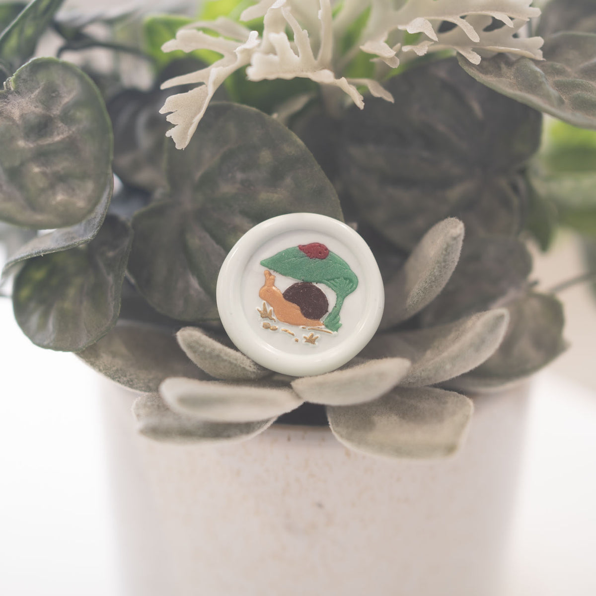 Snail under leaf with ladybug wax seal impression in gold wax close up