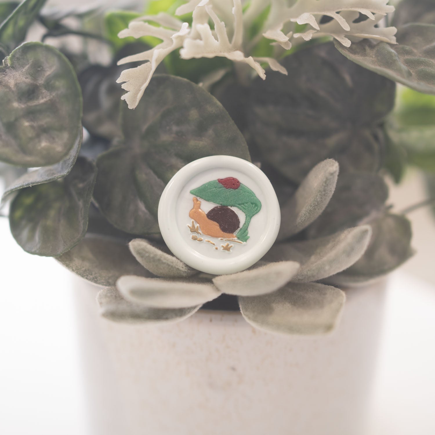 Snail under leaf with ladybug wax seal impression in gold wax close up