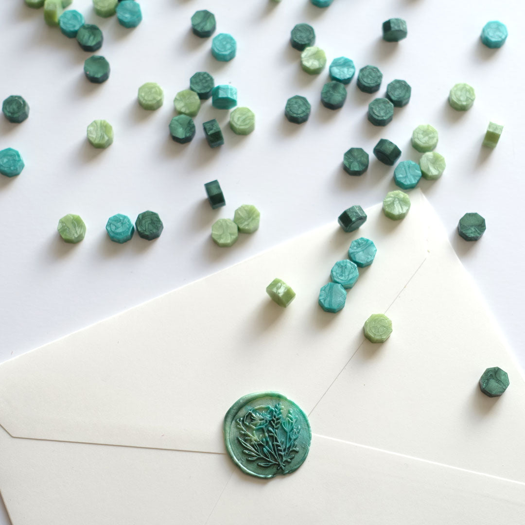 Mixed green wax beads pellets granules with wild flower wax seal on white envelope