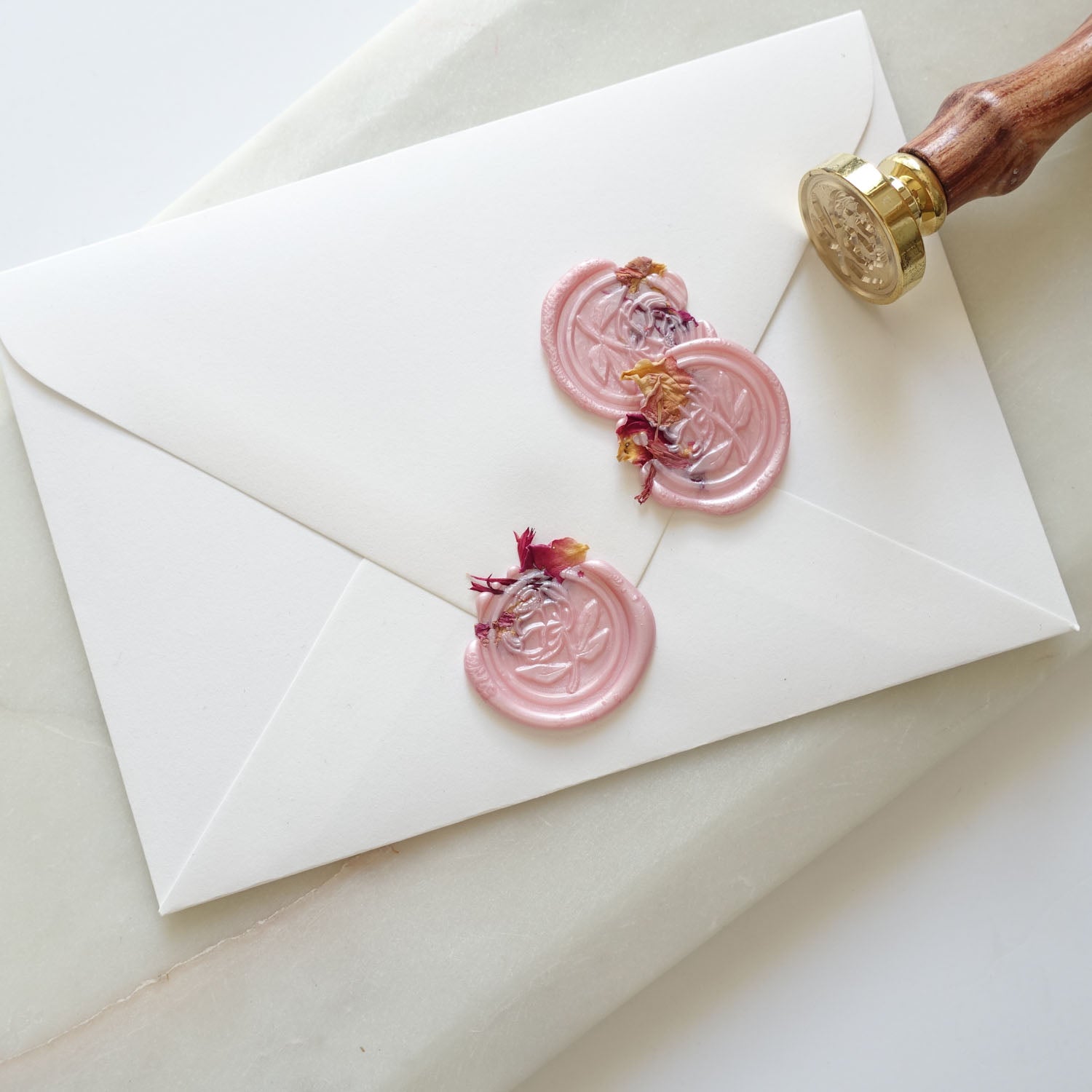 Blush pink sealing wax with peony wax seal and rose petals on white envelope