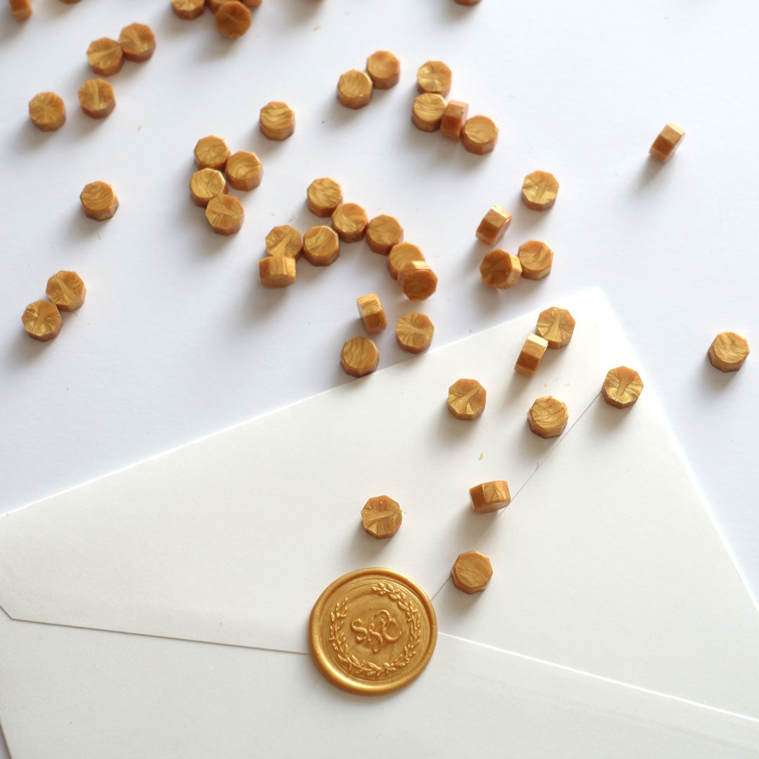 Yellow gold wax beads pellets granules with monogram wreath wax seal on white envelope